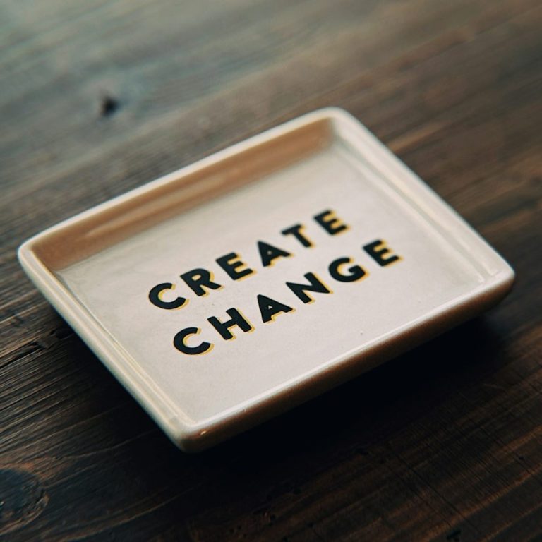 Create Change Keramikplatte mit der Aufschrift „CREATE CHANGE“ in goldenen Buchstaben.